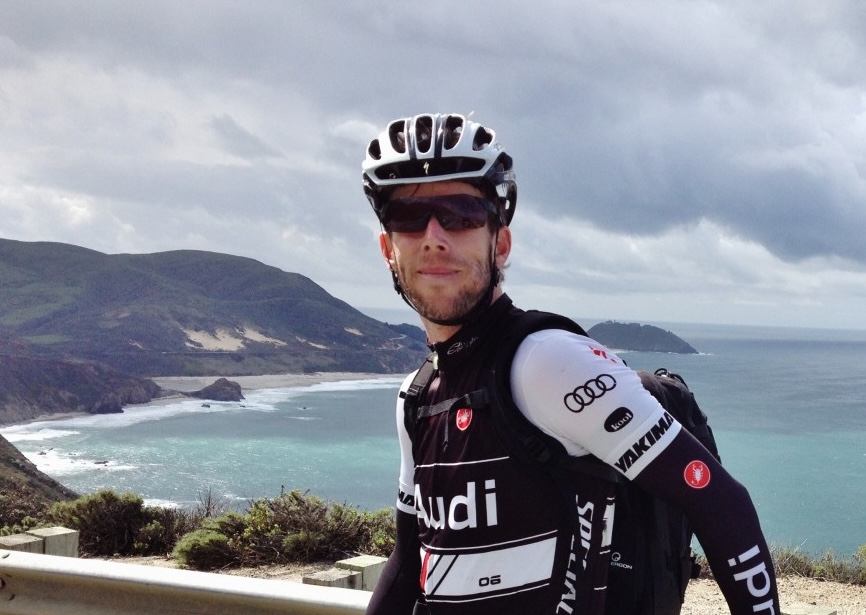 A man dressed in spandex and helmet stands above Big Sur coastline.